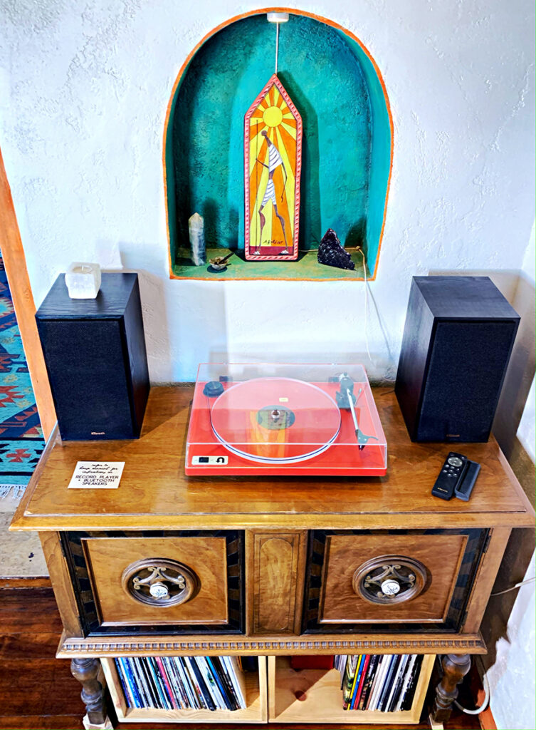 Turquoise niche in wall with orange art and red record player on antique buffet